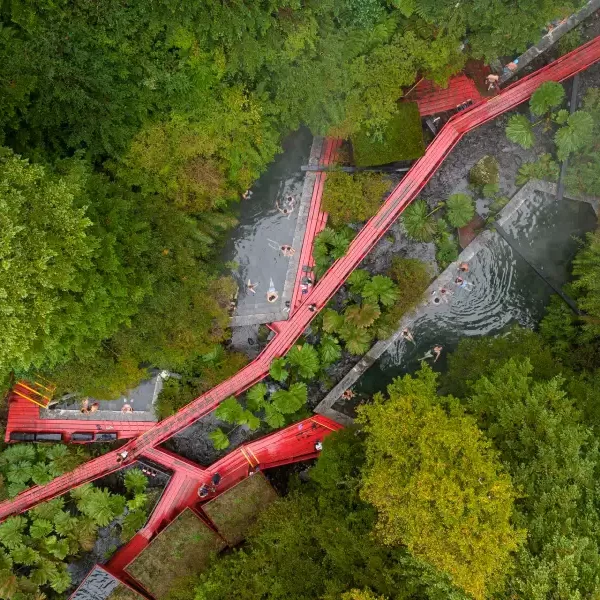 “Pasarelas rojas características de las Termas Geométricas rodeadas de naturaleza.”