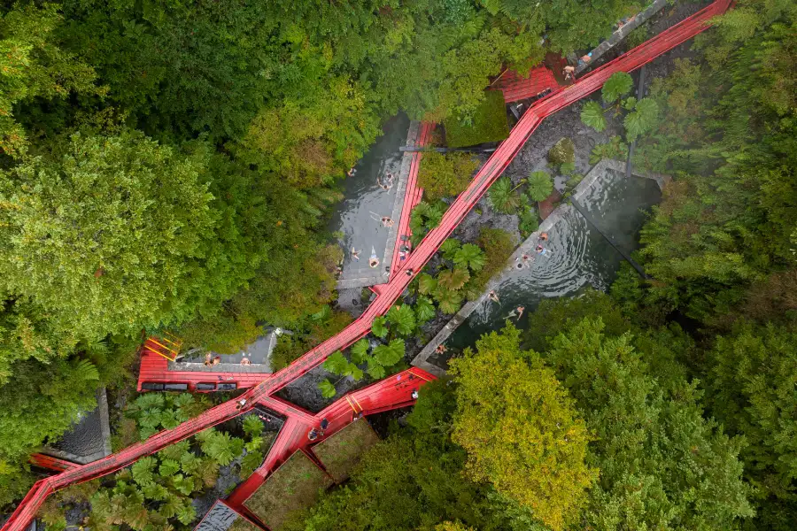 “Pasarelas rojas características de las Termas Geométricas rodeadas de naturaleza.”